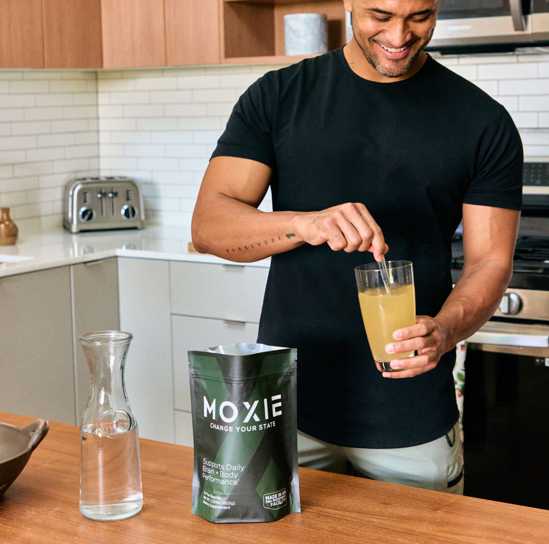 Photo of athletic man in a kitchen stirring Moxie in a glass of water. Energy and mood bost from one scoop.